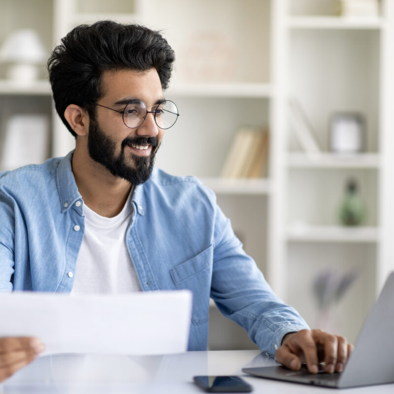 Jeune homme devant un ordinateur avec un papier à la main