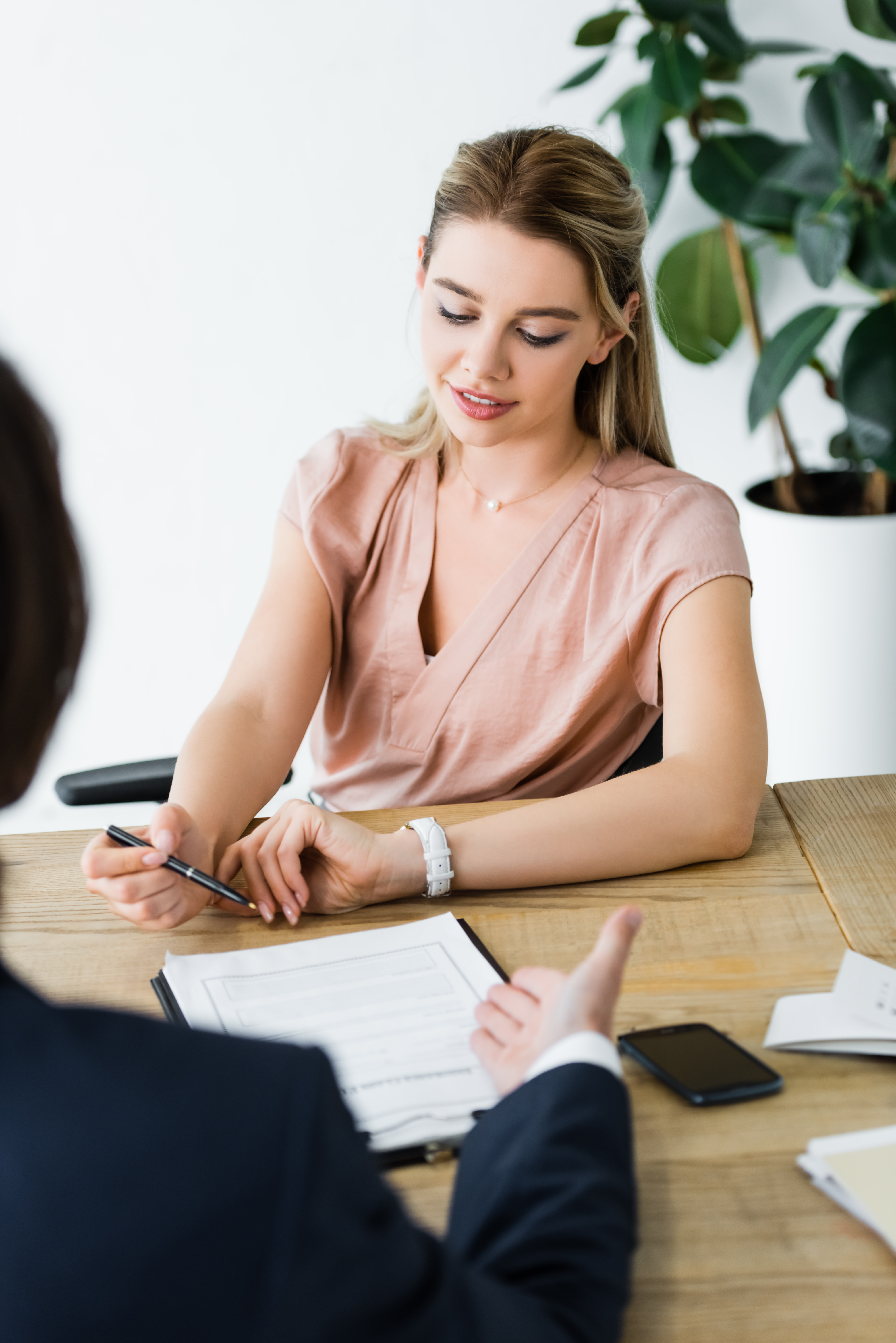 Une jeune femme souriante va signer un document que lui présente un homme de dos