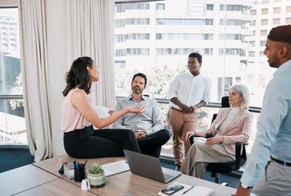 1 femme fait une présentation à 4 autres personnes, dans un cadre de bureau