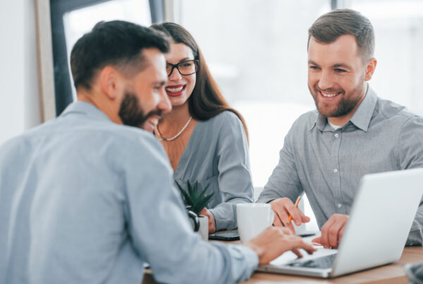 Photo de 3 personnes dans un environnement de travail, qui regardent un ordinateur.