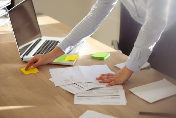 Photo d'un bureau avec des documents et post-it, où les bras d'une femme sont visibles