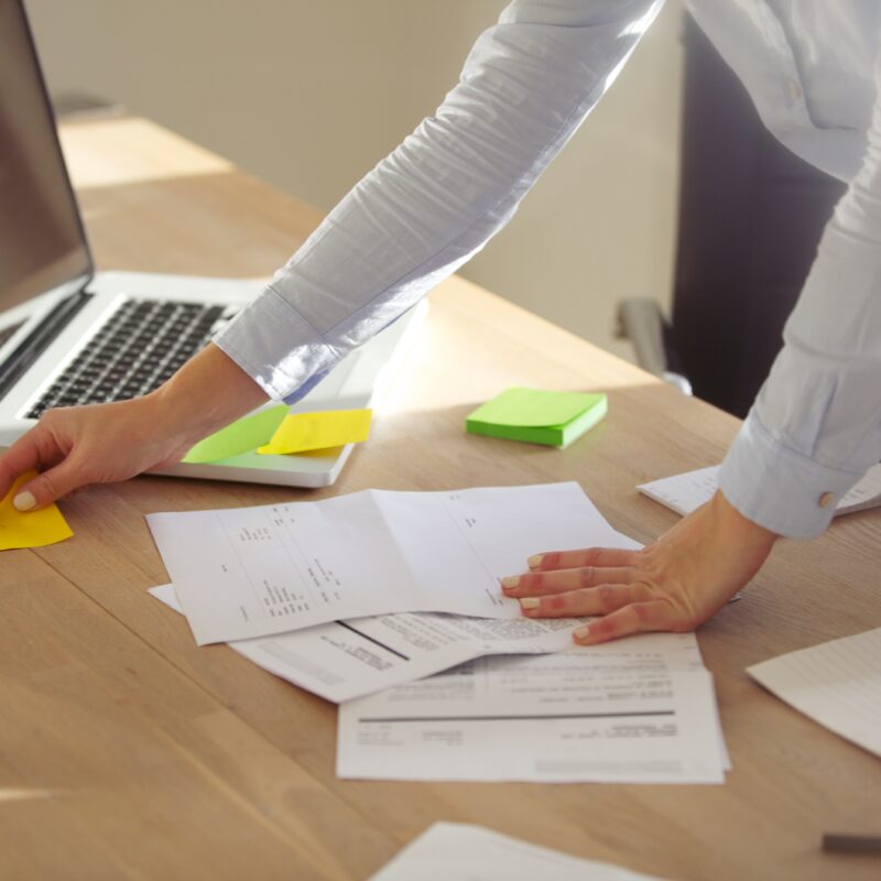 Photo d'un bureau avec des documents et post-it, où les bras d'une femme sont visibles